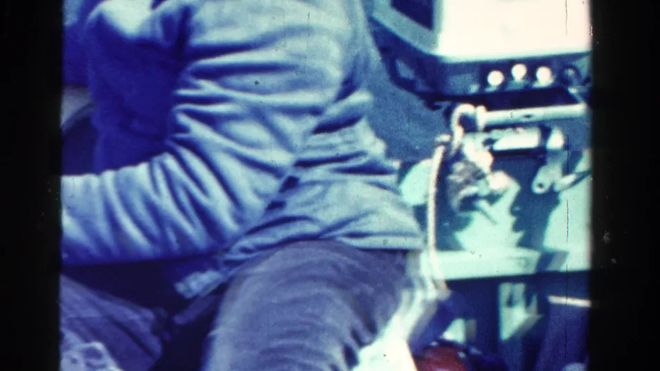 Close handheld view inside the small boat, showing the rower’s clothing, oar fittings, and lake surface in the 1958 Ontario clip.