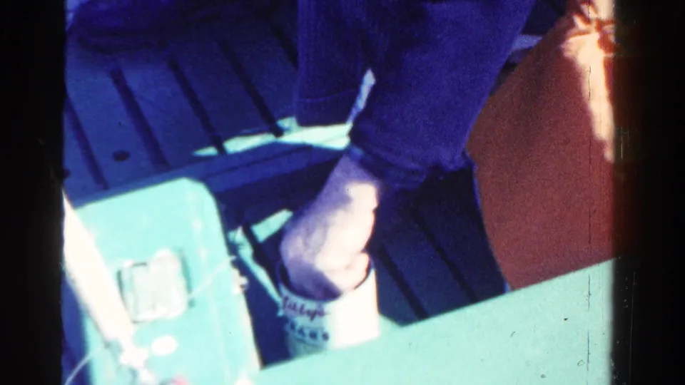 A close 1958 Ontario boat view shows the fisherman's hand near a cup with partial text and a light-colored tackle box.