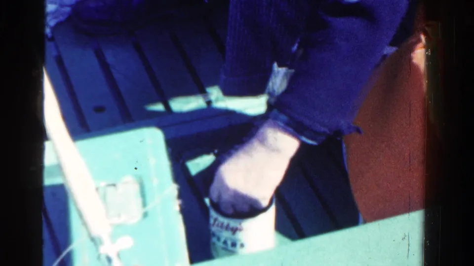The 8mm frame shows the fisherman's hand and sleeve beside a cup, tackle box hardware, and greenish boat surfaces.
