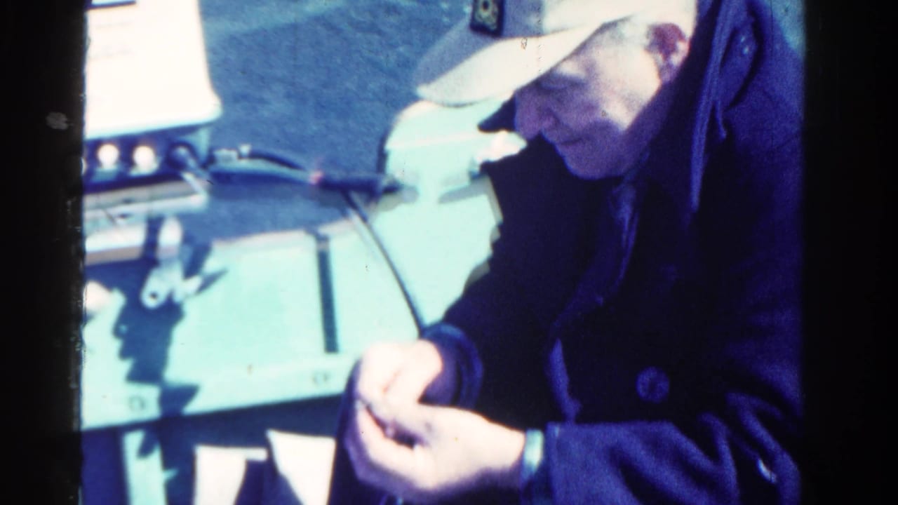 Man in a cap looking down at his hands inside a small boat.
