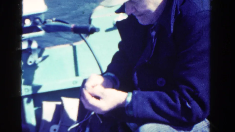 The 8mm frame shows the man still working with a small item beside pale boat hardware and open water in Ontario.