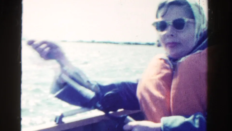 In the final frame, the woman in a headscarf, sunglasses, and orange life vest gestures beside the boat rail on open water.