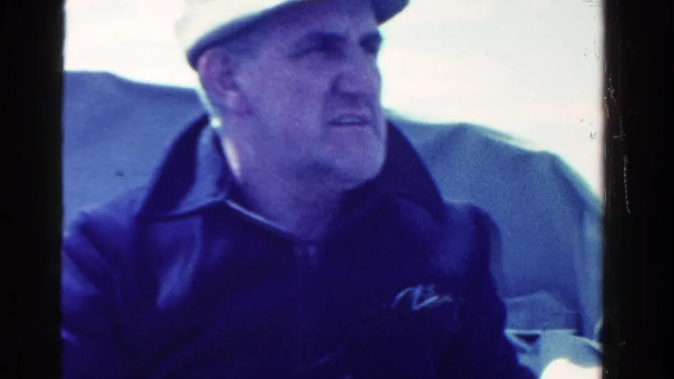 A seated man in a cap and dark jacket appears aboard the boat in the 1958 Ontario home-movie footage.
