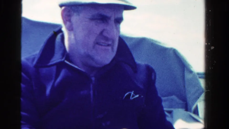 In the Ontario, Canada boating clip, a man in a cap and dark jacket sits near cushioned boat seats in bright daylight.