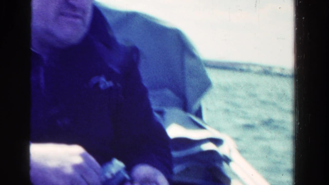 Man in dark clothing seated in a small boat beside open water.
