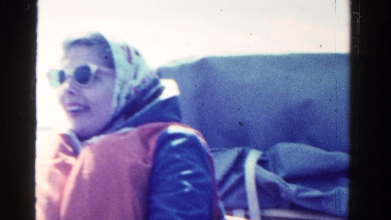 Woman in sunglasses, headscarf, and life vest sits on a boat in bright sun.