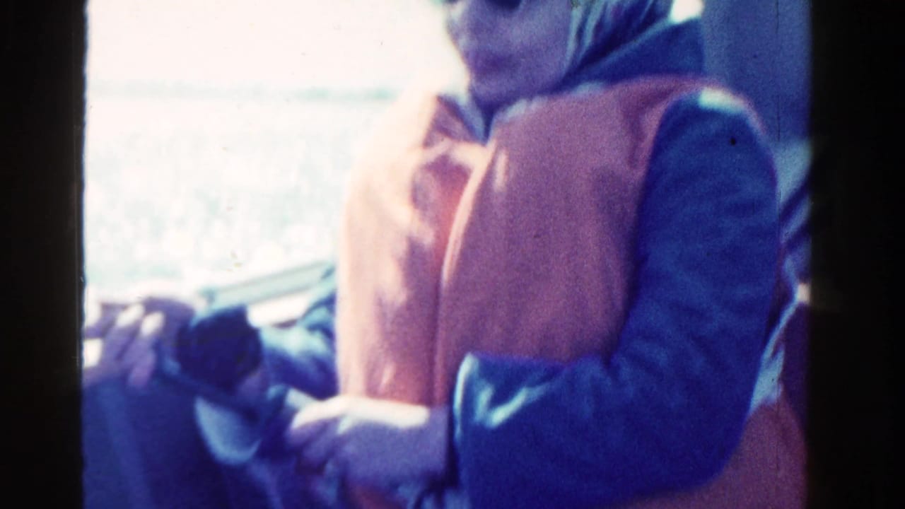 Woman on a boat holds fishing gear while wearing a life vest and headscarf.