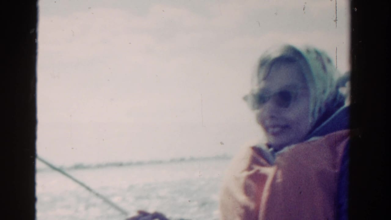 The woman sits near a fishing line on the boat, with water and bright sky visible in the 1958 Ontario home movie.