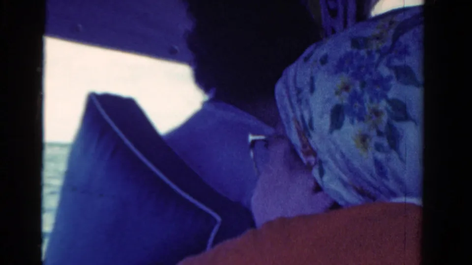 1958 Ontario 8mm frame showing a seated boat passenger in a patterned headscarf, partly framed by the boat and lake.