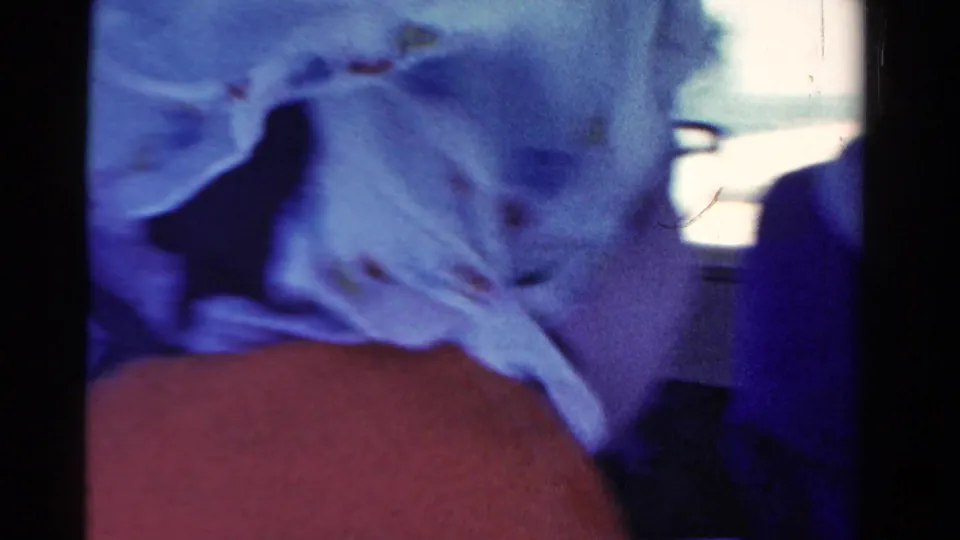 Close 1958 Ontario home-movie frame of a boat passenger in a light patterned headscarf, with another person at the edge of the shot.