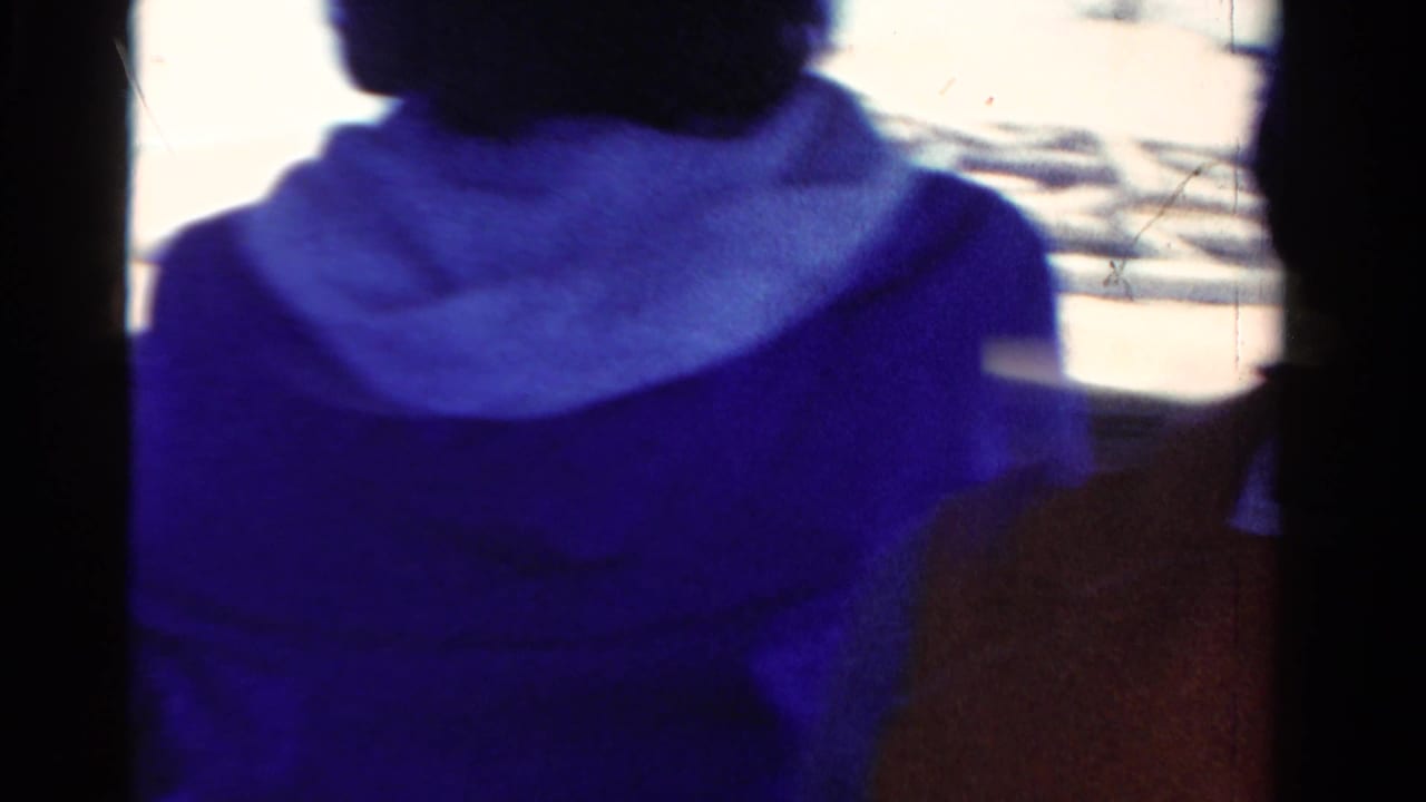 Cropped 1958 Ontario 8mm frame showing a woman in blue clothing seated on a boat in bright daylight.