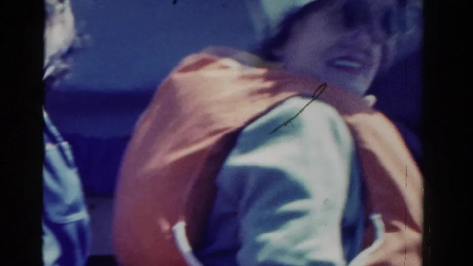 A woman in an orange life vest smiles back toward the handheld camera during the 1958 Ontario boating scene.