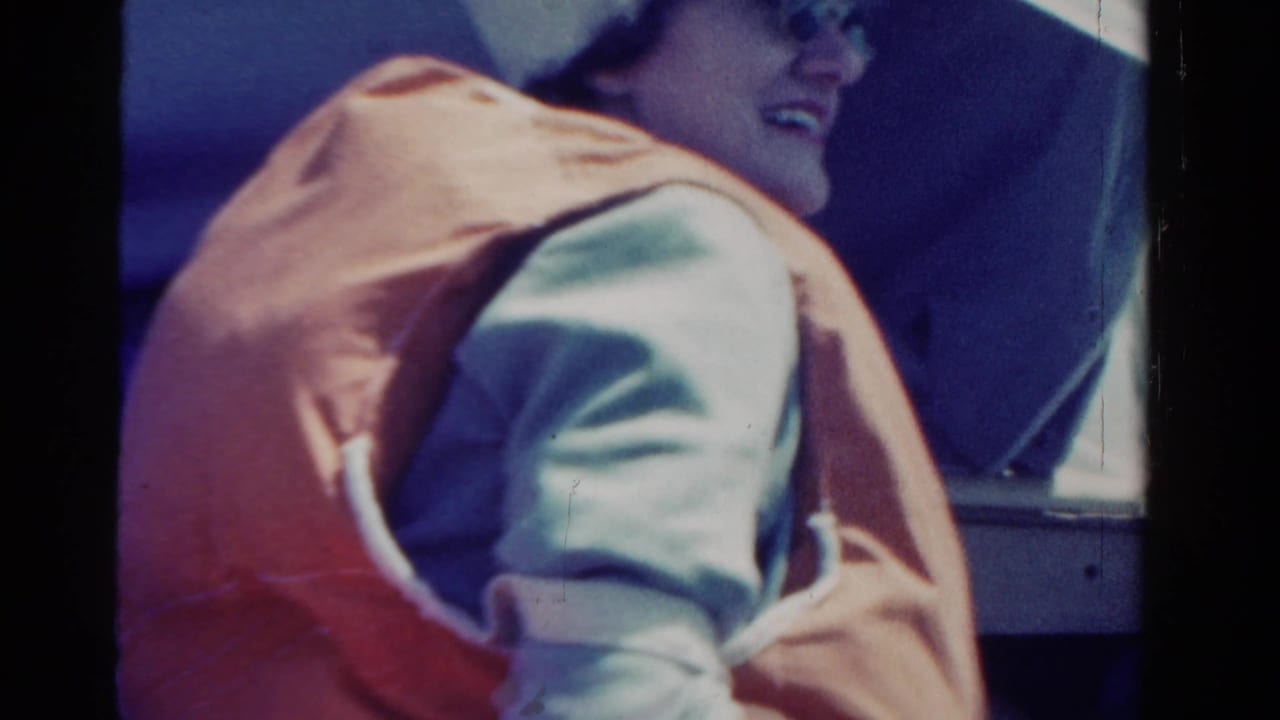 In supported 1958 Ontario home-movie footage, a woman in sunglasses and an orange life vest smiles while seated on a boat.