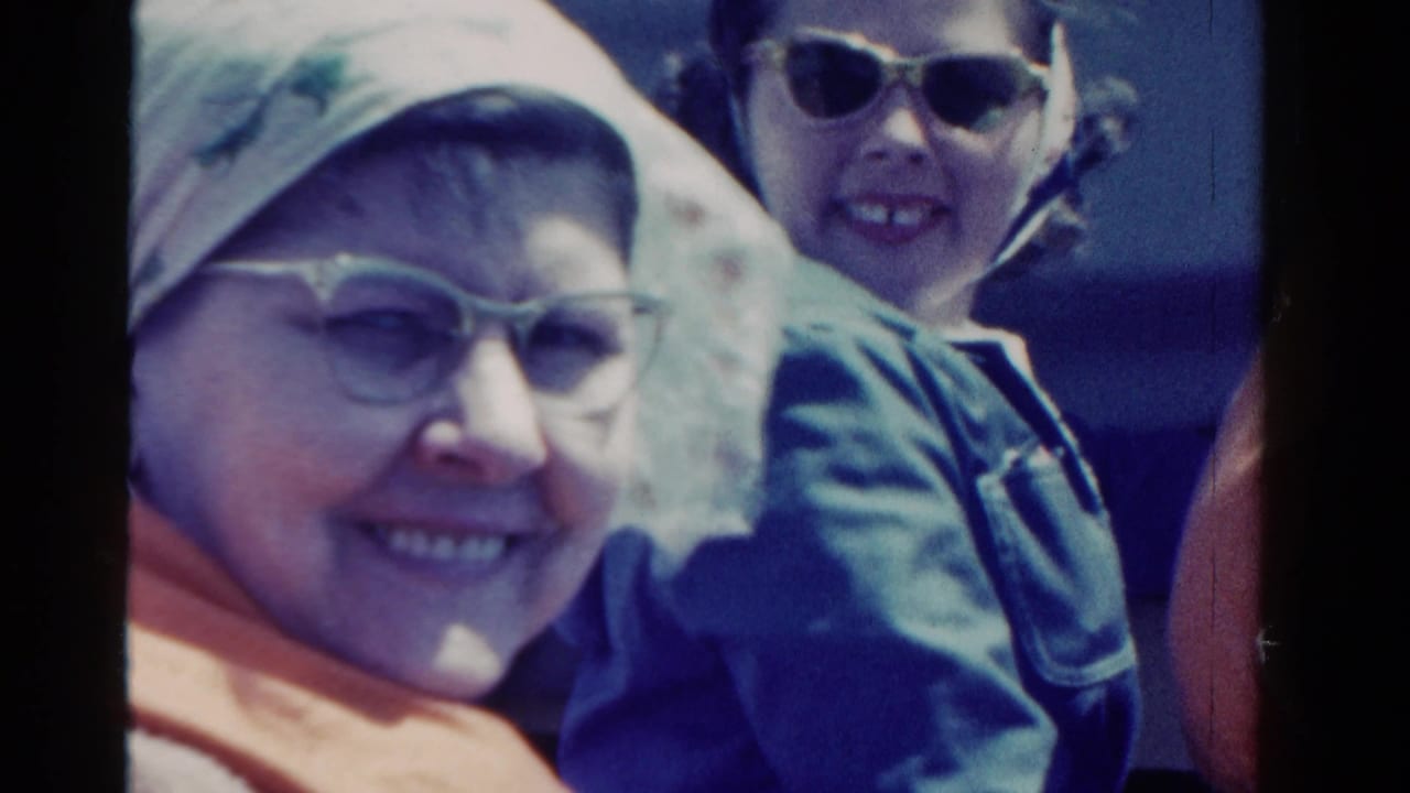 Two people smile toward the camera on a boat in the supplied 1958 Ontario home-movie footage, with life vests and sunglasses visible.