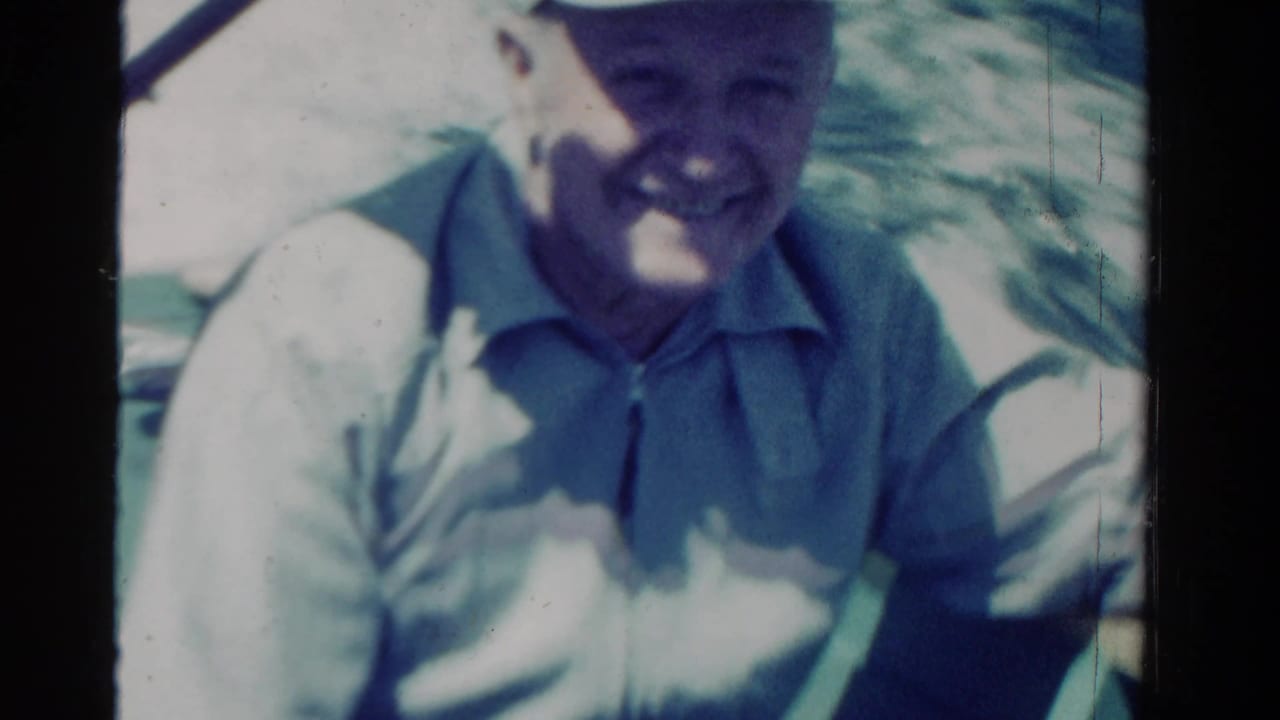 In this 1958 Ontario home-movie frame, a smiling man in a white cap sits on a boat in bright sun.