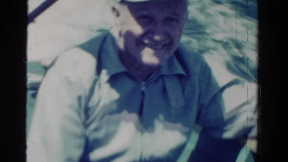 In this 1958 Ontario home-movie frame, a smiling man in a white cap sits on a boat in bright sun.