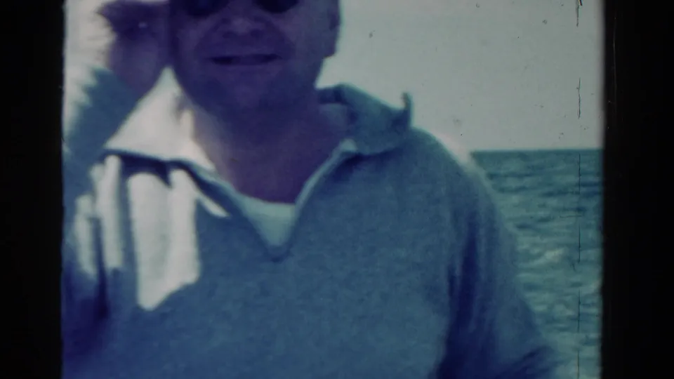 Adult man in a light cap and collared shirt faces the camera on a boat in supported 1958 Ontario home-movie footage.