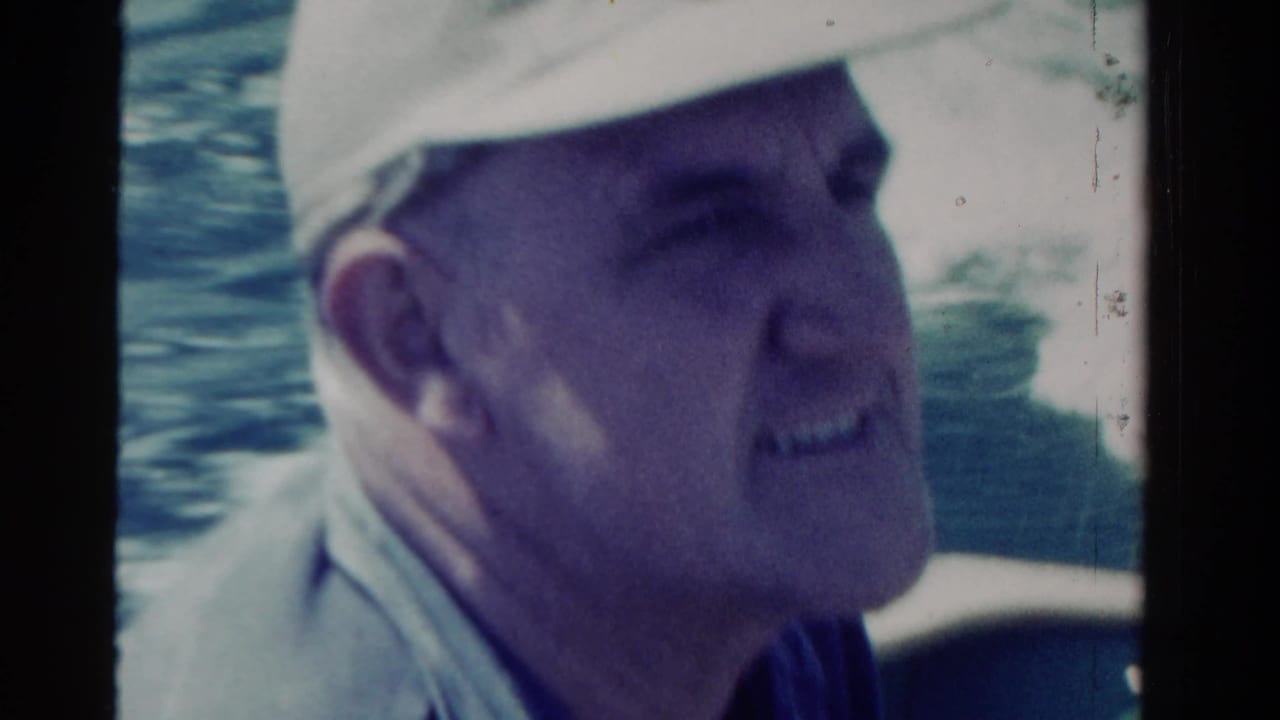 Close side view of a man in a light cap on a boat with water in the background.