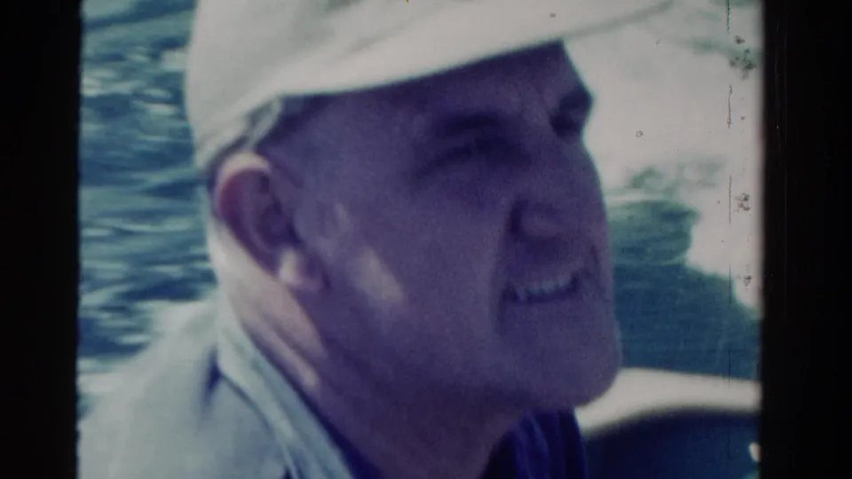 Close side profile of a man in a light cap aboard a boat, with water behind him in 1958 Ontario footage.