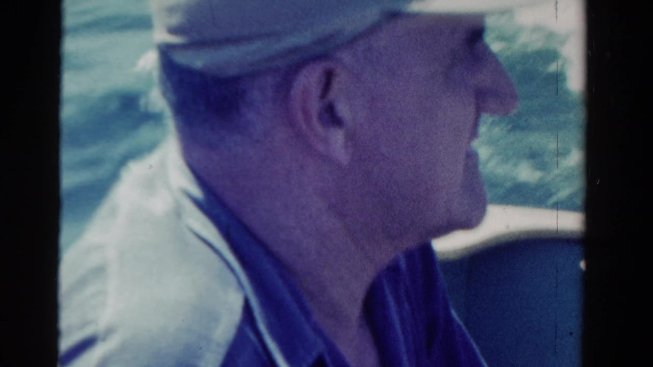Man in profile wearing a cap while riding on a boat near open water.