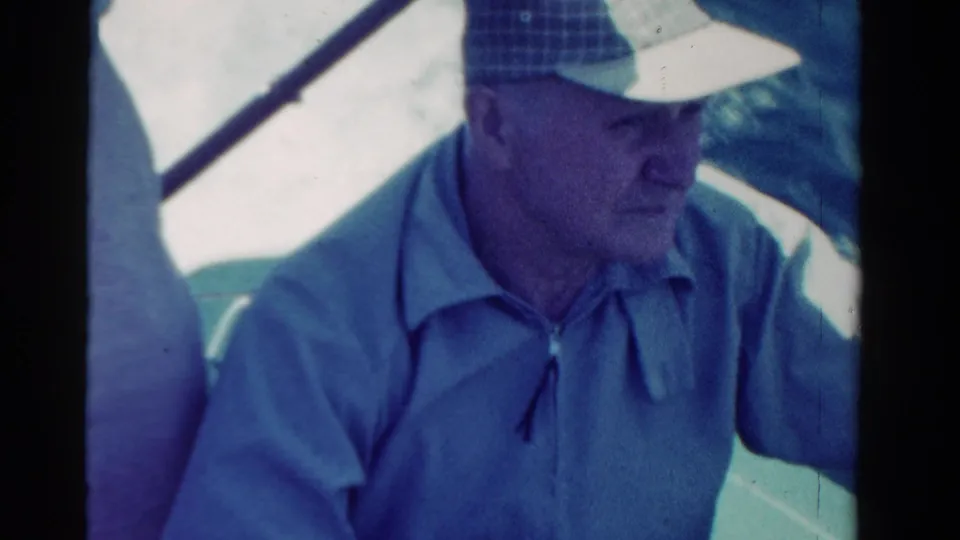 Adult male passenger in a checkered cap and blue shirt appears in a 1958 Ontario road-trip home-movie frame.