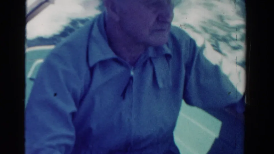 Close 8mm frame of an adult male passenger in a cap inside a car, consistent with the 1958 Ontario road-trip metadata.