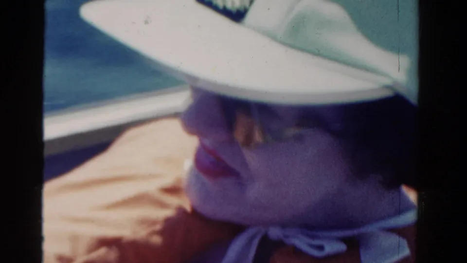 Adult woman wearing a white hat smiles from inside the car in this 1958 Ontario home-movie road-trip frame.