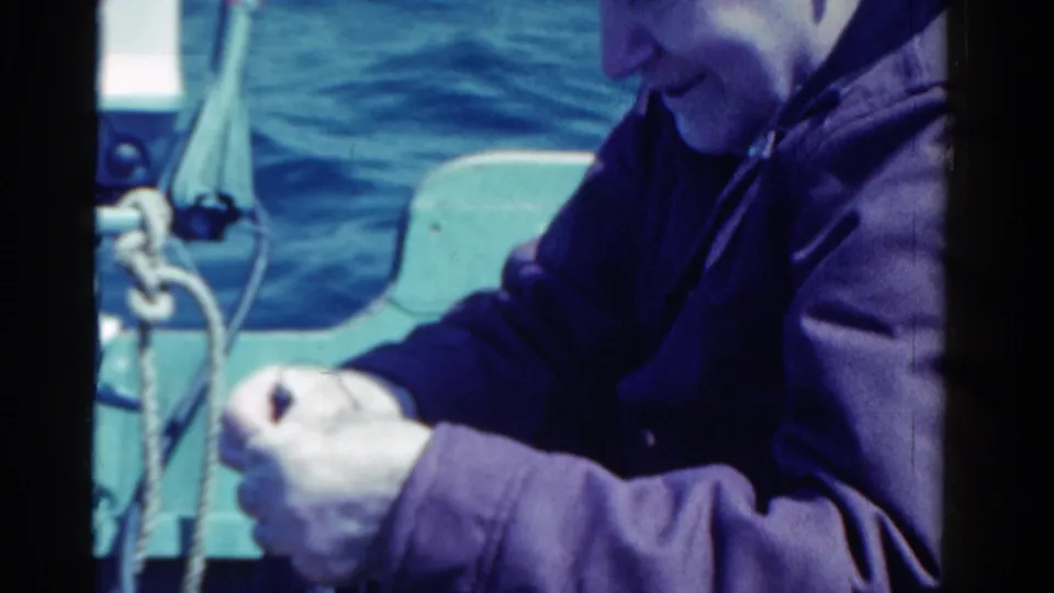 1958 Ontario home-movie frame showing a man on a boat handling a fishing line or hook, with water and boat hardware in view.
