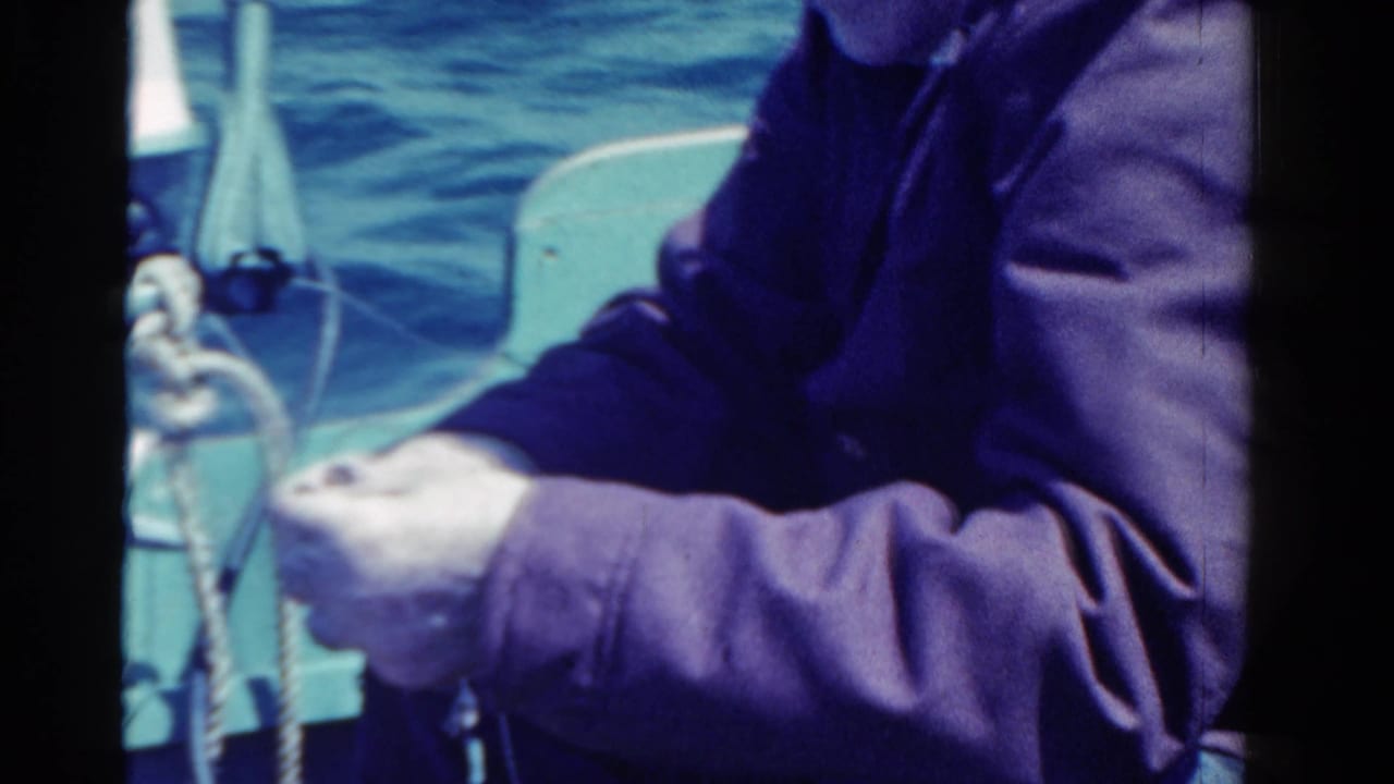 1958 Ontario home-movie frame of a man on a small boat handling rope, with open blue water behind him.