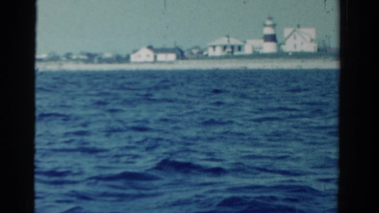Distant Ontario shoreline in 1958, with a lighthouse and low white buildings seen across choppy water from a boat.