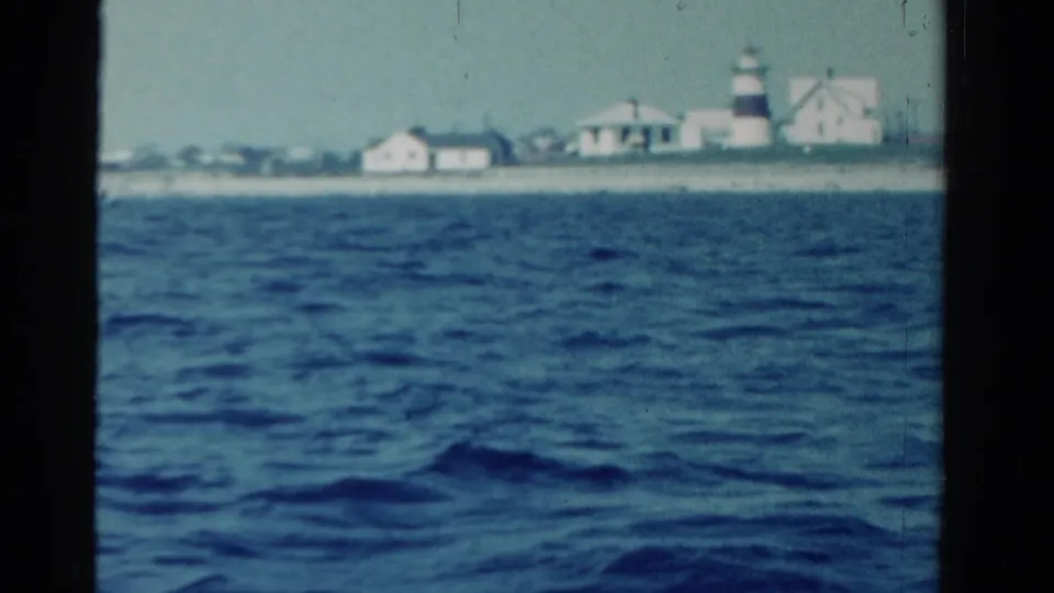 Distant Ontario shoreline in 1958, with a lighthouse and low white buildings seen across choppy water from a boat.