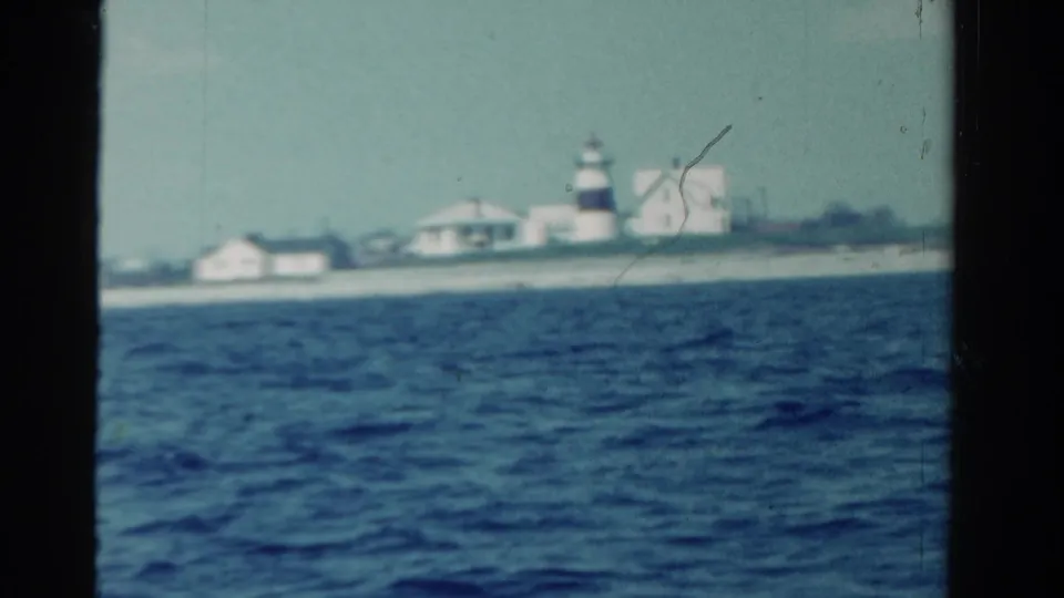 Soft 8mm frame of an Ontario coastal shoreline, showing a lighthouse and pale buildings beyond open water.