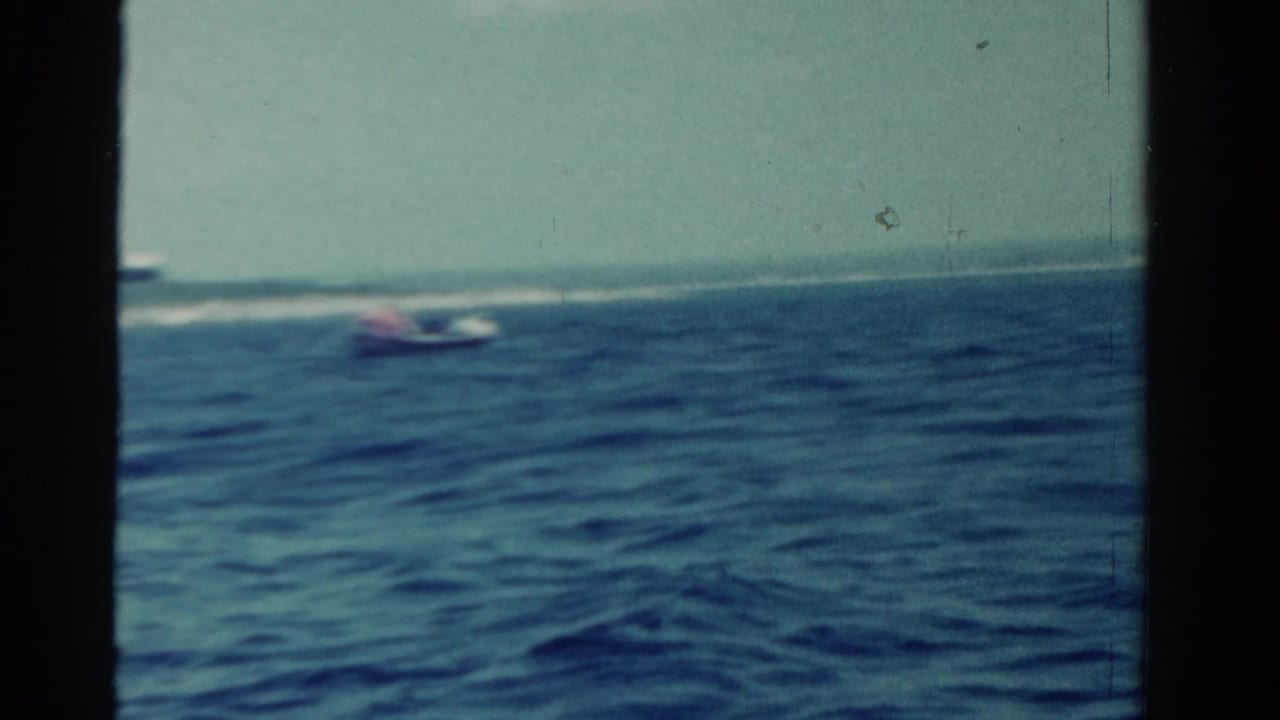 1958 Ontario 8mm frame showing small boats moving across open water, with a low distant shoreline and soft home-movie color.