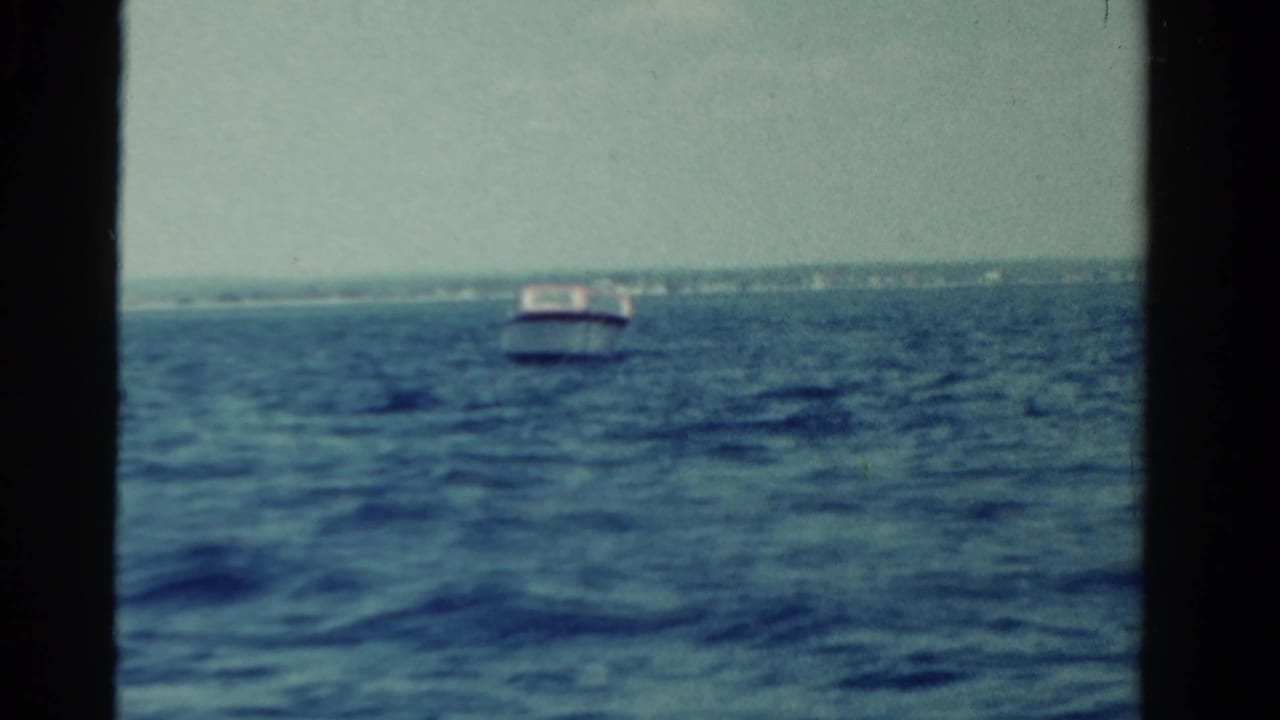 A small boat sits on open water with shoreline visible across the horizon.