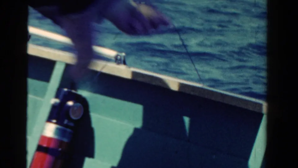 1958 Ontario 8mm frame from inside a boat, showing railing, choppy water, a red-and-silver fire extinguisher, and a hand pulling a line.