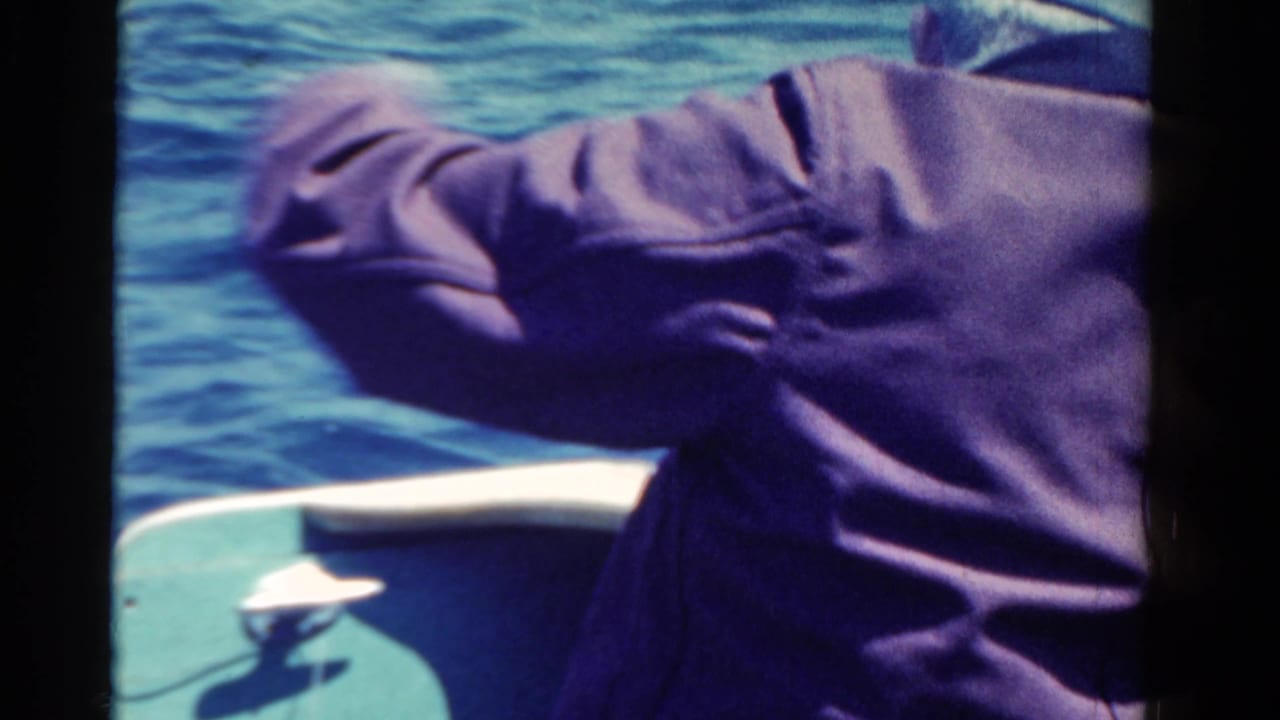 Man seen from behind on a boat with fishing line extending toward the water.
