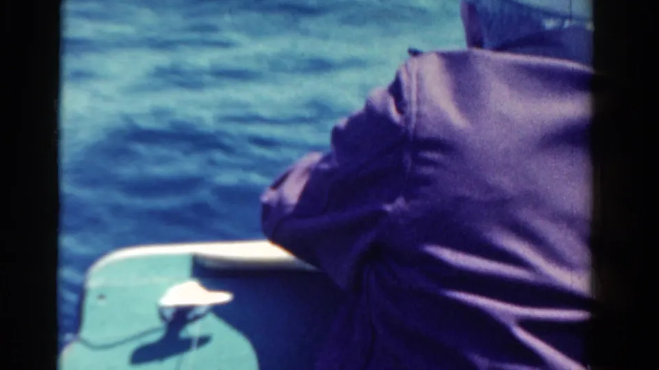 A 1958 Ontario boating frame shows the man from behind, partly cropped, with the boat edge and open water visible.