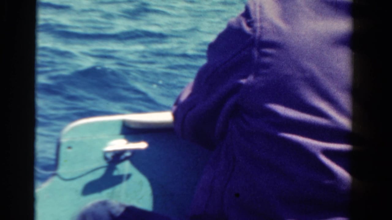 1958 Ontario home-movie frame showing a person from behind in a small boat on rippling blue water.
