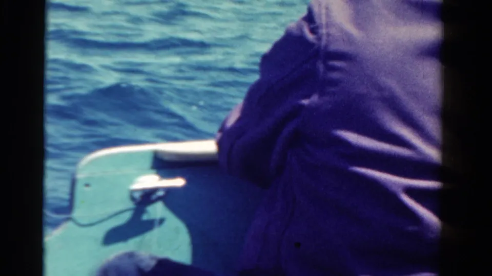 1958 Ontario home-movie frame showing a person from behind in a small boat on rippling blue water.