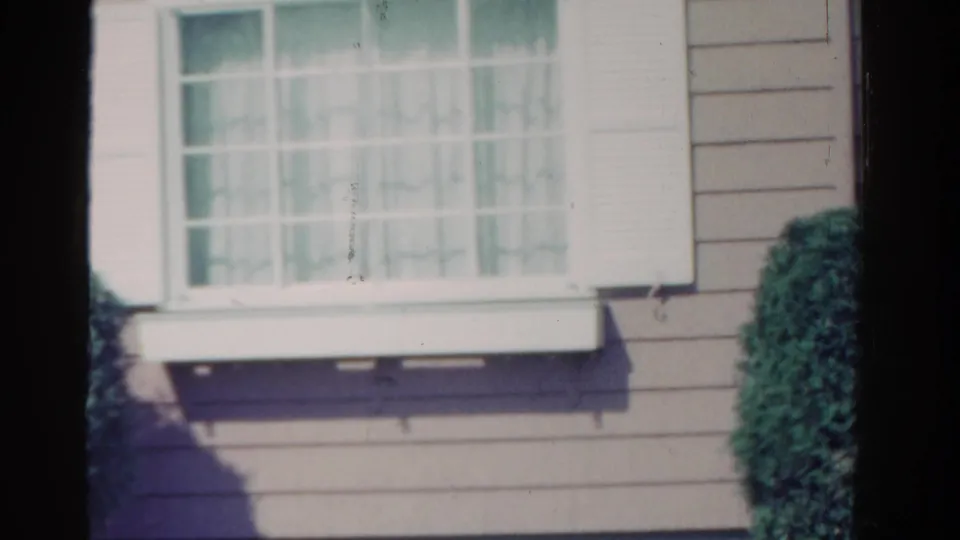 1958 Ontario home exterior with a white-trimmed window, light siding, window box or ledge, shadow, and shrubbery.