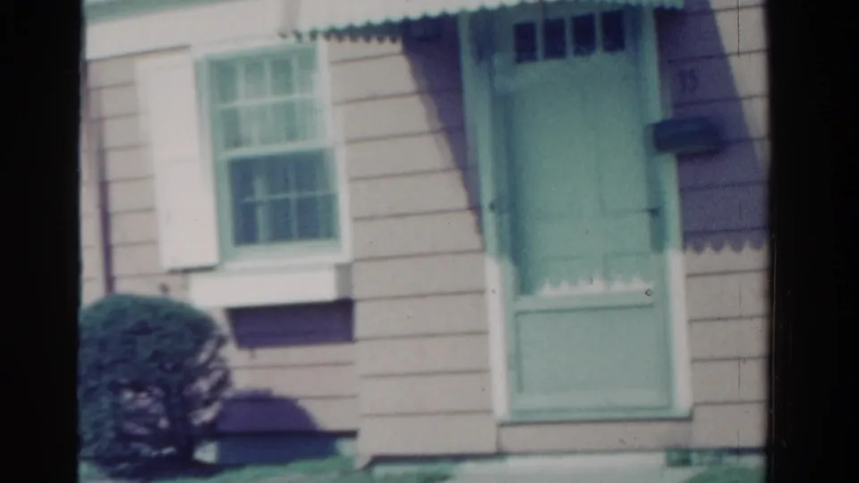 End of the 1958 Ontario house pan showing the green door, adjacent windows, clapboard siding, shrub, and porch trim.
