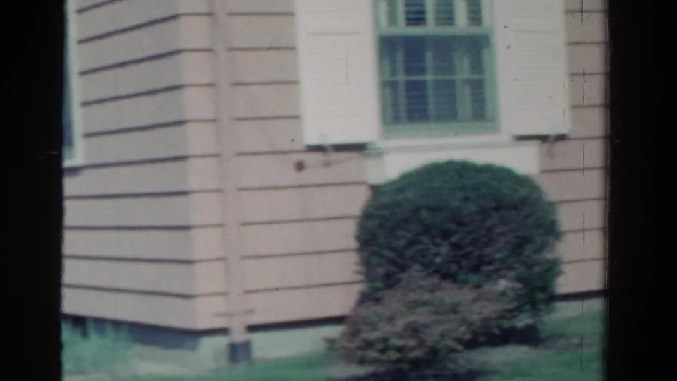 1958 Ontario home exterior showing a clapboard corner, shuttered window, green lawn, trimmed shrub, and low foundation.