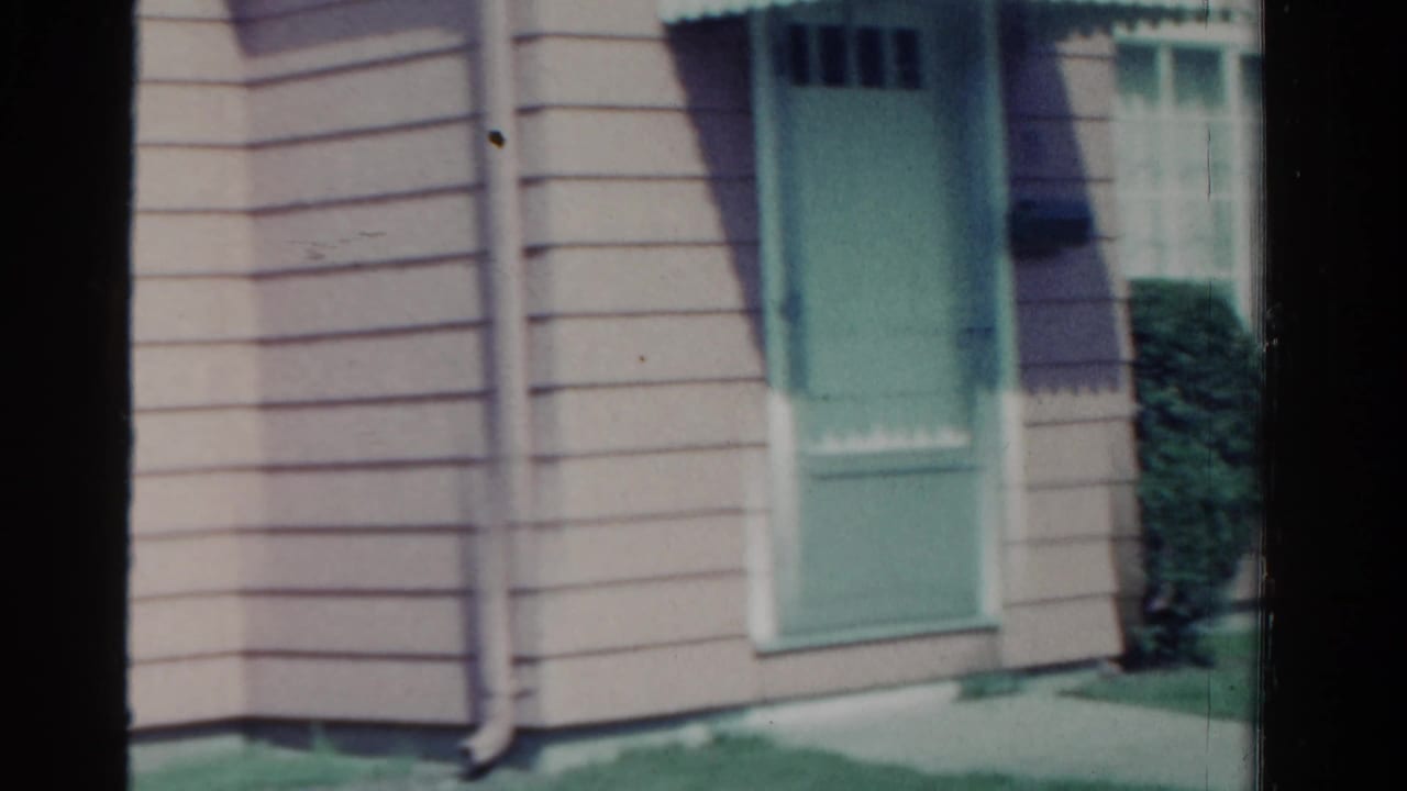 Beige-sided house with mint-green door, window, shrubs, and lawn.