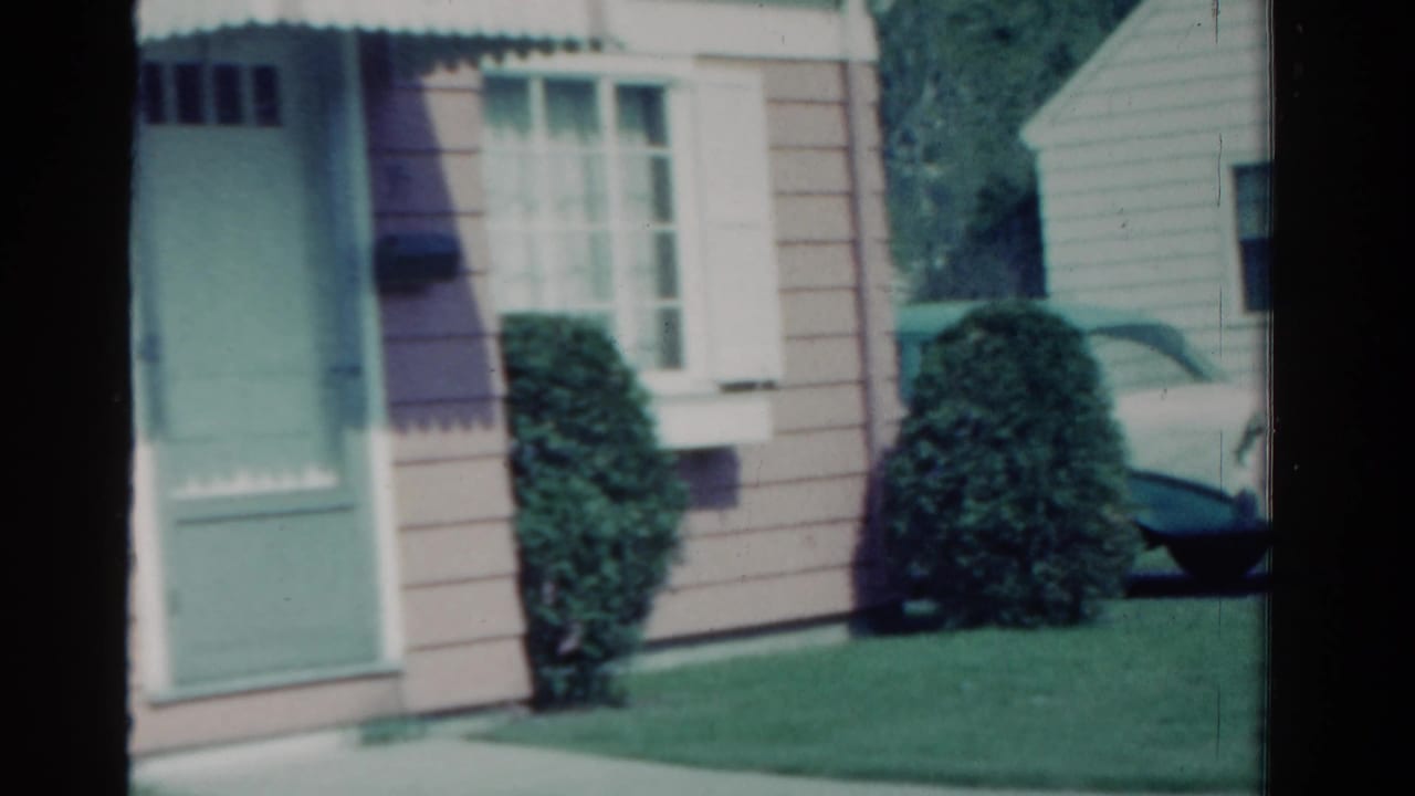 1958 Ontario suburban exterior with a mint-green door, white-framed window, shrubs, lawn, and part of a white car at the right edge.