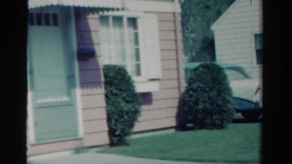1958 Ontario suburban exterior with a mint-green door, white-framed window, shrubs, lawn, and part of a white car at the right edge.