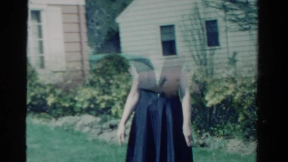 1958 Ontario garden view with a woman in a dark sleeveless dress partly obscured by film damage or exposure near a beige house exterior.