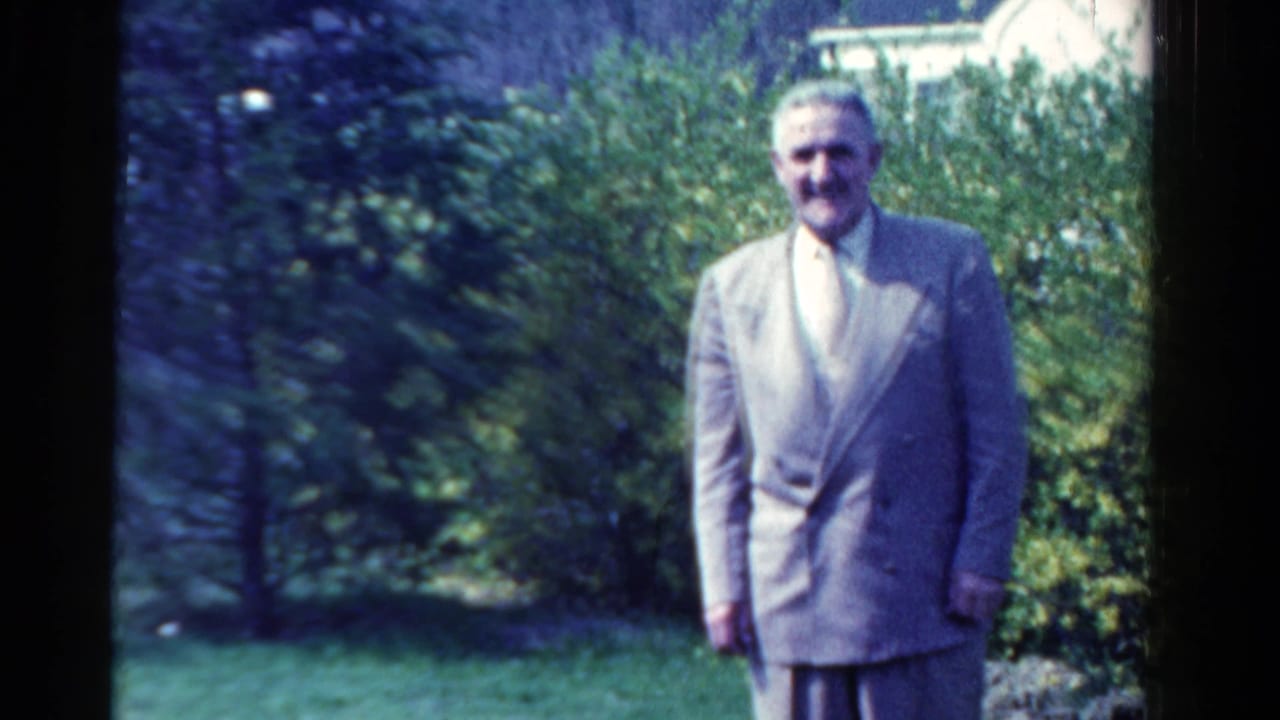 Adult man in a light suit and tie poses in an Ontario garden in 1958 home-movie footage.