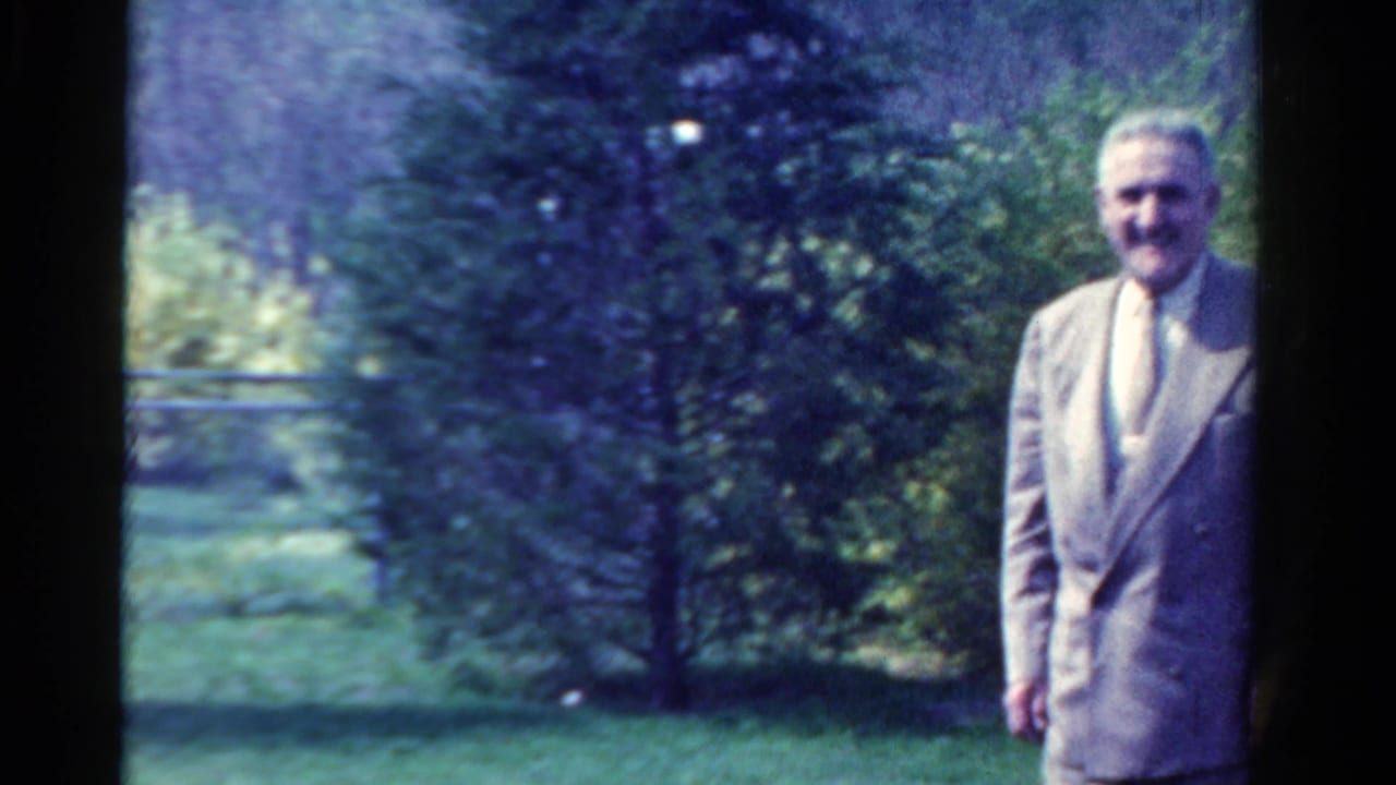 The suited man is partly framed at the right edge of a 1958 Ontario garden scene on 8mm film.