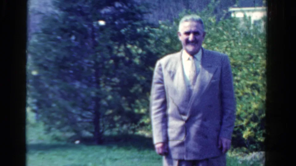 A suited adult man stands front-facing in an Ontario garden, consistent with the 1958 home-movie metadata.