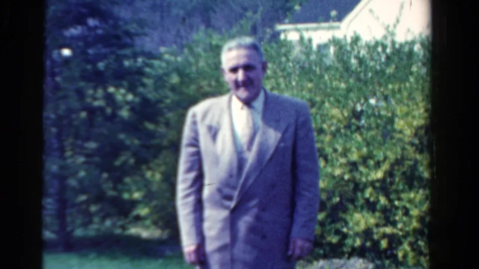 The 1958 Ontario 8mm frame shows a man in a light suit posing before thick garden shrubs.
